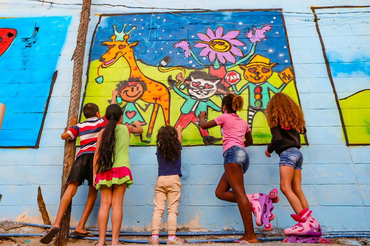 cinco crianças de frente para o mudo e de costas para a câmera olhando para os desenhos feitos 